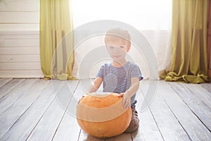 Wonderful little boy sitting with big pumpkin. Children celebrate Halloween in interior of living room. Happy halloween