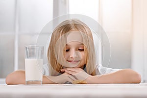 Wonderful little girl with blonde hair sits near milkglass.