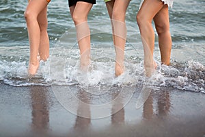 Wonderful long-legged women are walking near the sea on the sand. A cute sports women`s legs.
