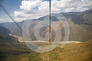 Wonderful panoramic view into Chicamocha Canyon with river bed, white clouds and blue sky with cables of aerial cable car,