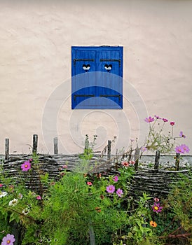 Wonderful house in the countryside with blue window shutters and small openings shaped like little hearts behind flower garden