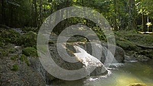 Wonderful scenery of water stream flowing from cascade through the rock into a small natural pond under sunlight.