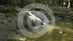 Wonderful scenery of water stream flowing from cascade through the rock into a small natural pond under sunlight.