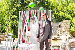 Wonderful stylish rich happy bride and groom at a wedding ceremony in green garden near wedding arch