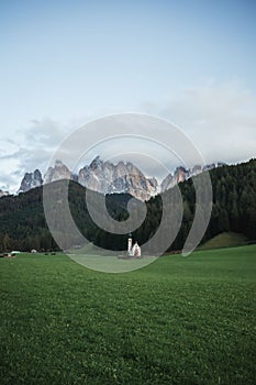Sunny Landscape of Dolomite Alps with St Johann Church and mountains in the background