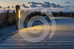Wonderful sunrise over a wooden path with lanterns alongside, North Sea coast, Netherlands