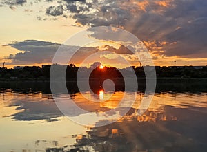 Wonderful sunset over the city horizon with reflection on the calm lake water in a silent summer evening