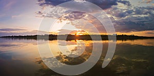 Wonderful sunset panorama over the city horizon with reflection on the calm lake water in a silent summer evening