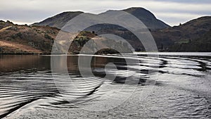 Wonderful Winter landscape image viewed from boat on Ullswater in Lake District with unusual water ripple wake movements