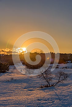 Wonderful winter orange sunset in snow-covered field with the sun closed by clouds. Russia, Stary Krym.