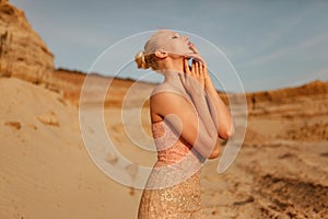 Wonderful woman in splendid slim gold dress posing in desert at the sunset. Profile portrait of a sensual model