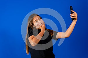Wondering little cute girl surprised with an interesting information on mobile smartphone. Isolated on blue background.