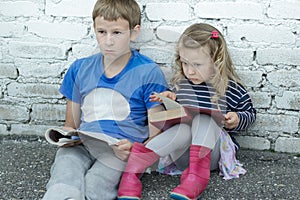 Wondering sibling children sitting on asphalt ground with books in hands