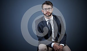 He wont lose focus. Studio portrait of a handsome young businessman sitting on a chair against a dark background.