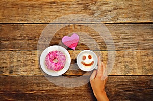 Wood background with cup of coffee, donut, heart and woman`s han