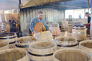 Wood barrels production cooper using hammer and tools in workshop