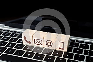 Wood block symbol telephone, mail, address and mobile phone on laptop keyboard. Website page contact us