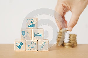 Wood blocks with healthcare medical icon , blurred hand and stack of coins for health insurance, wellness, wellbeing concept