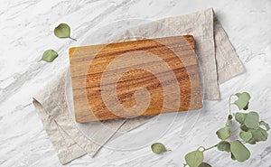 Wood board on linen napkin on marble kitchen table with green leaves