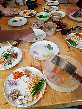 Wood board table cooking together ingridients plate ax knifes pad thai onions spring roll thai food tofu carotte asian photo