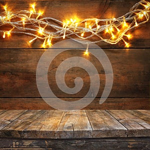 Wood board table in front of Christmas warm gold garland lights on wooden rustic background. filtered image. selective focus