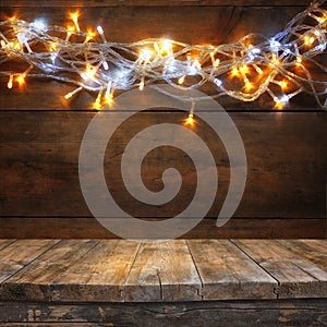 Wood board table in front of Christmas warm gold garland lights on wooden rustic background. filtered image. selective focus