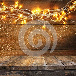 Wood board table in front of Christmas warm gold garland lights on wooden rustic background. filtered image. selective focus.