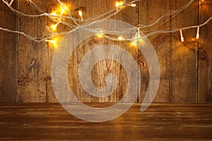 wood board table in front of Christmas warm gold garland lights on wooden rustic background. glitter overlay