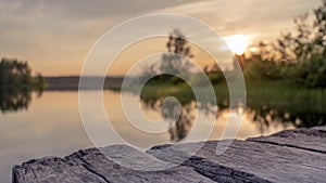 wood board table in front of sanset landscape of sparkling lake water. background is blurred.