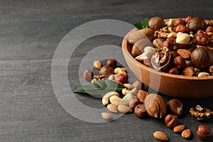 Wood bowl with different tasty nuts on gray wooden background