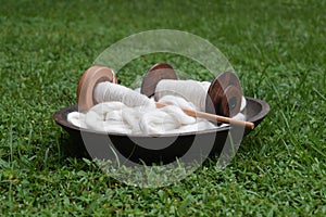 Wood bowl filled with white cotton roving and a spindle and a bobbin on a green grass background