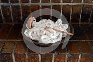 Wood bowl filled with white cotton roving and a spindle on a brick background