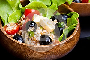 Wood bowl with spelt salad with olives and tomatoes