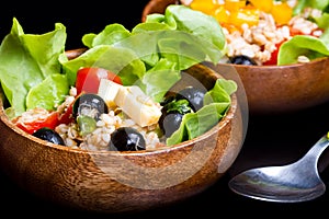 Wood bowl with spelt salad with olives and tomatoes
