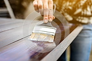 Wood carpenter applies a protective layer of transparent varnish. Hand with a brush close up on the table top