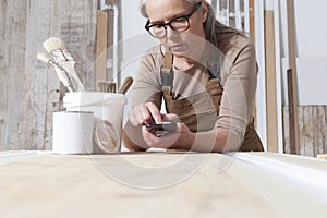 Wood crafts, woman artisan carpenter with mobile phone search the internet in her workshop, restoration, diy and handmade works