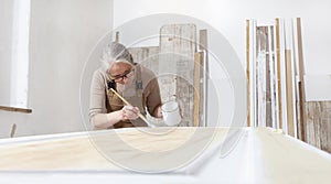 Wood crafts, woman artisan carpenter painting with brush and paint jar white the door in workshop, wearing overall and eyeglasses