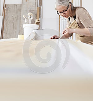 Wood crafts, woman artisan carpenter painting with brush and paint jar white the door in workshop, wearing overall and eyeglasses