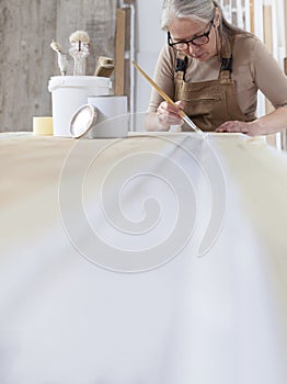 Wood crafts, woman artisan carpenter painting with brush and paint jar white the door in workshop, wearing overall and eyeglasses