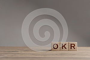 Wood cubes with acronym `OKR` - `Objectives and Key Results` on a beautiful wooden table, studio background. Business concept