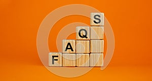 Wood cubes with word `FAQS` stacking as step stair on beautiful orange background, copy space. Business concept