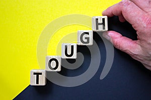 Wood cubes with word `tough` stacking as step stair on paper yellow and black background, copy space. Male hand. Business concep