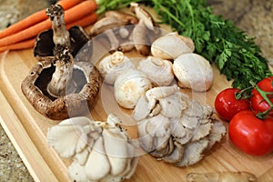 Wood cutting board in kitchen table with fresh ingredients carrot, mushroom, potatoes, tomatoes, food many colors orange, red.