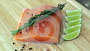 Wood cutting board in kitchen table with fresh red salmon fish salt pepper and lime ready to cook.