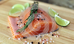 Wood cutting board in kitchen table with fresh red salmon fish salt pepper and lime ready to cook.