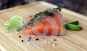 Wood cutting board in kitchen table with fresh red salmon fish salt pepper and lime ready to cook.