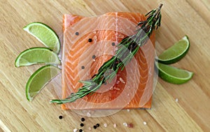 Wood cutting board in kitchen table with fresh red salmon fish salt pepper and lime ready to cook.