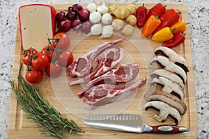 Wood cutting board in kitchen table with raw lamb ribs red meat, rosemary, mushrooms, tomatoes, cheese, onions and peppers.