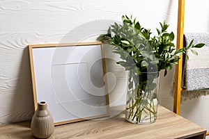 Wood empty frame with copy space, plant in pot on table and towel hanging against white wall