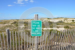 wood fence and sand dunes at the beach with please keep off sign